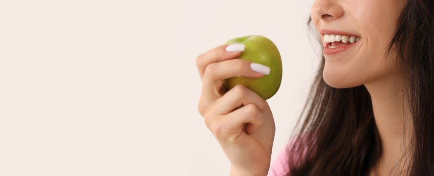 Young woman with healthy white teeth smiling while holding a fresh green apple, promoting healthy eating and dental care
