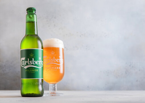 LONDON,UK - DECEMBER 08,2025: Bottle and glass of Carlsberg lager beer on light table background.