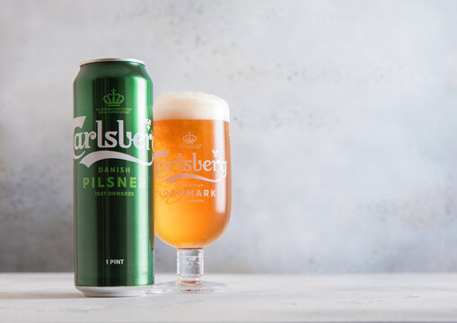 LONDON,UK - DECEMBER 11,2025: Aluminium tin and original glass of Carlsberg lager beer on light table background.