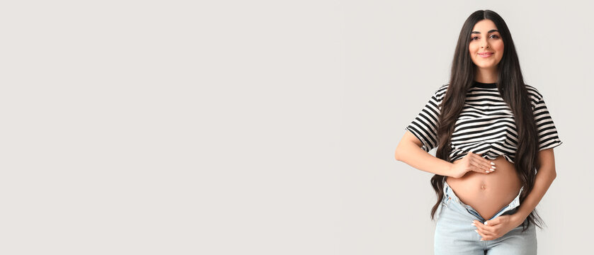 Young pregnant woman with long dark hair showing her bare belly and unbuttoned jeans, maternity and new life