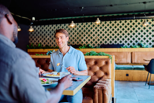 Two diverse friends enjoying lunch together, smiling and talking at a modern restaurant booth