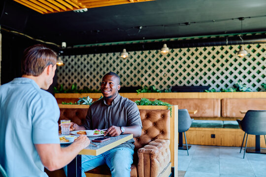 Diverse men enjoying lunch and conversation in a modern restaurant interior, showing business networking and friendship