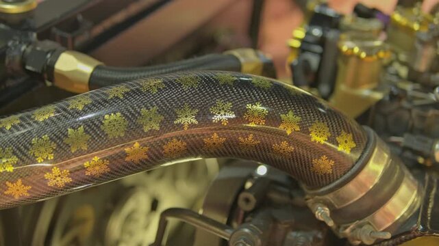 Close-up of a custom carbon fiber turbo intake pipe decorated with metallic gold snowflake patterns in a high-performance engine bay.