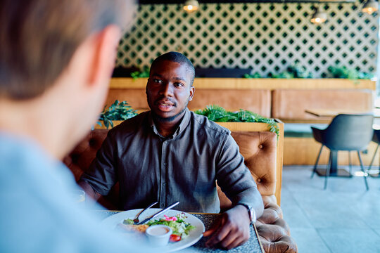Young Black man talking with someone off-frame during a casual business lunch meeting in a modern restaurant