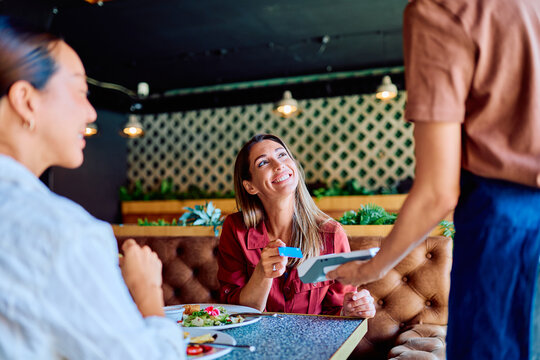 Woman smiling, paying for a meal with a credit card using a payment terminal after dining in a stylish cafe