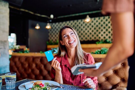 Happy woman smiling while paying her bill with a credit card at a restaurant, using a payment terminal