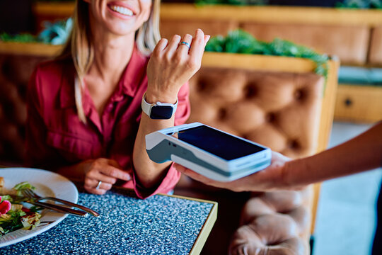 Woman using a smartwatch for contactless payment at a restaurant, showing modern digital transaction convenience