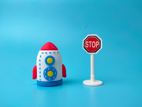 A toy rocket positioned next to a miniature octagonal red stop sign on a blue background