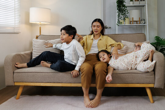 Asian mother and her two children sitting on a sofa in the living room, sharing a peaceful moment and enjoying family time at home