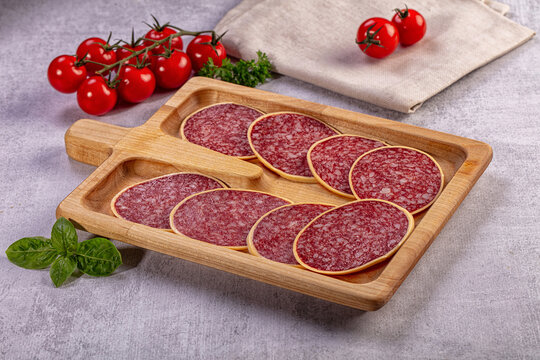 Sliced salami in cheese on wooden board with tomatoes and basil