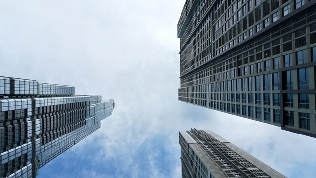 Worm's eye view of modern skyscrapers framing a cloudy sky, showcasing geometric facades, vertical lines, urban density, and contemporary city architecture.