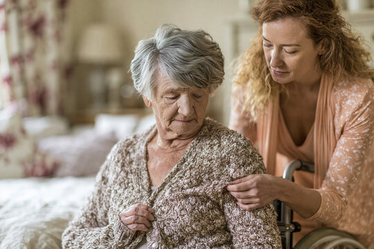 Adult daughter helping elderly mother button cardigan indoors