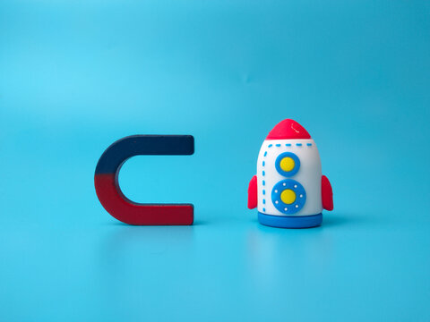 A toy rocket positioned next to a blue and red horseshoe magnet on a blue surface
