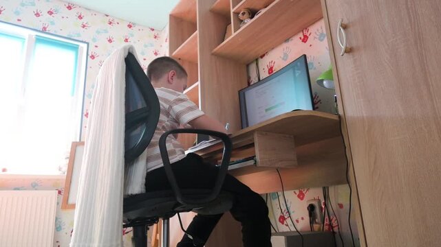 Focused Young Schoolboy Studying and Doing Homework on Computer at His Desk at Home