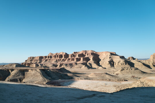 Camels Walking Past Mudstone Hills in Arid Desert Landscape
