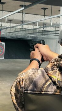Man Practicing Shooting at Indoor Range, Person in camo attire aiming a handgun at targets in a shooting range, focusing on precision and safety.
