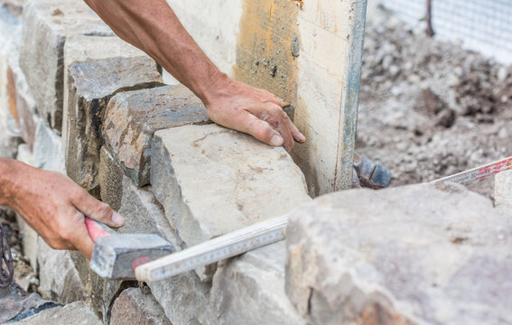 Building a brick wall of natural stone, with hammer, handmade, close-up of human hands