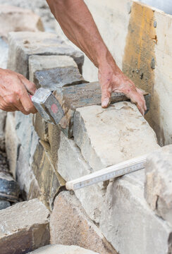 Building a brick wall of natural stone, with hammer, handmade, close-up of human hands
