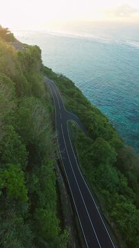 Vertical video. Smooth Cinematic Aerial Flight Along Coastal Road At Pantai Tanah Barak, Wide Angle Sunrise View Of Turquoise Ocean And Forested Cliffs In Golden Light, Travel And Freedom