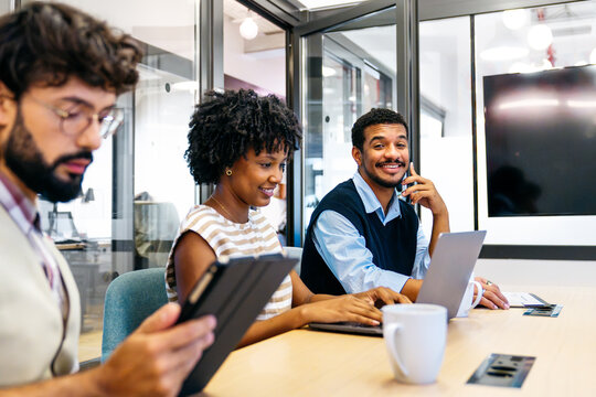 Diverse business people working together in a contemporary coworking office, smiling and using technology for collaboration