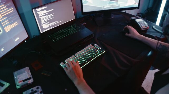 Young man in a headset hacking a security camera system in a dark room with computers