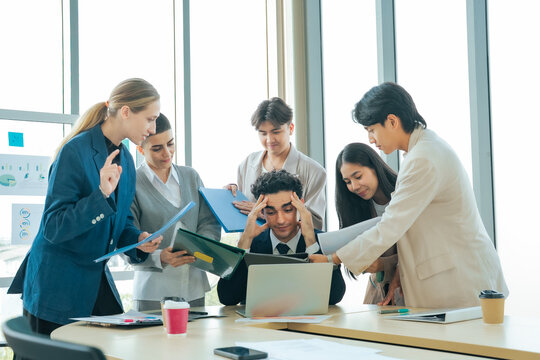 Business executive under pressure as colleagues explain reports and project updates around a laptop. Workplace stress, multitasking, office teamwork and deadline management in a busy company.