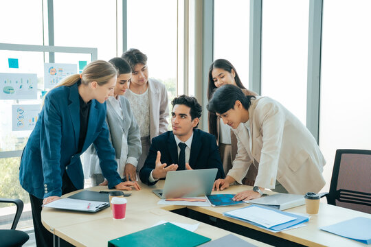 Multicultural business team exchanging ideas during a planning session around a laptop. Creative collaboration, teamwork and strategic communication in a bright modern office environment.