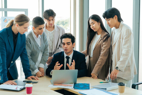 Busy office team reviewing reports and documents around a laptop during an important meeting. Corporate collaboration, project management and deadline preparation in a modern workplace.