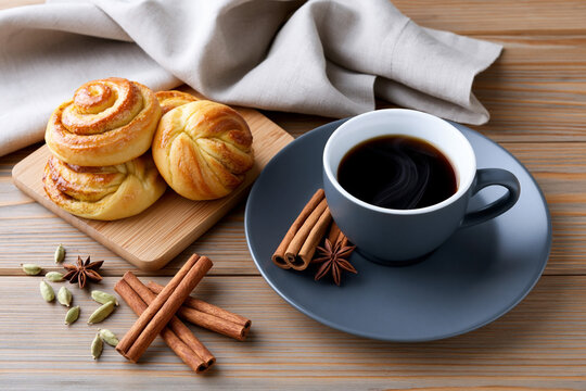 Fresh cinnamon rolls served with hot black coffee and aromatic spices on rustic wooden table for cinnamon roll day