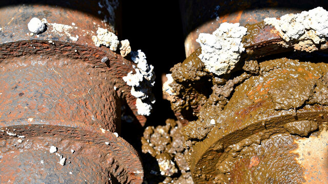 Close-up of corroded industrial pipes covered in thick mud and mineral deposits. Rusted metal flanges show signs of severe oxidation and wear. Industrial decay concept for engineering reports.