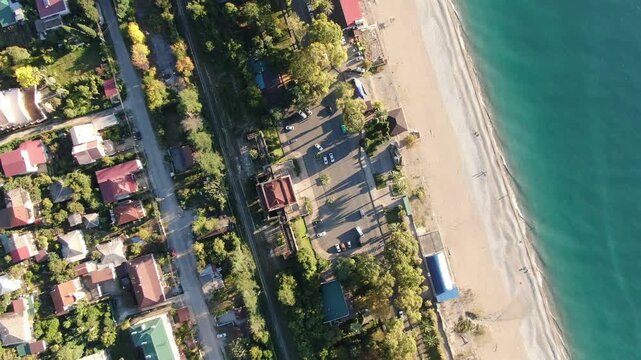 Top-down aerial view of the beach, coastline, and Black Sea in Gagra, Republic of Abkhazia, featuring nearby streets and buildings.