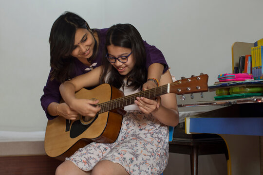 Mother helps her daughter play the guitar 