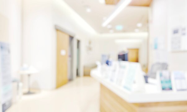 Blur abstract background of corridor in clean hospital. Blurry view of aisle in office with light floor. Defocus walkway in white light building hall with patient registration at reception desk.