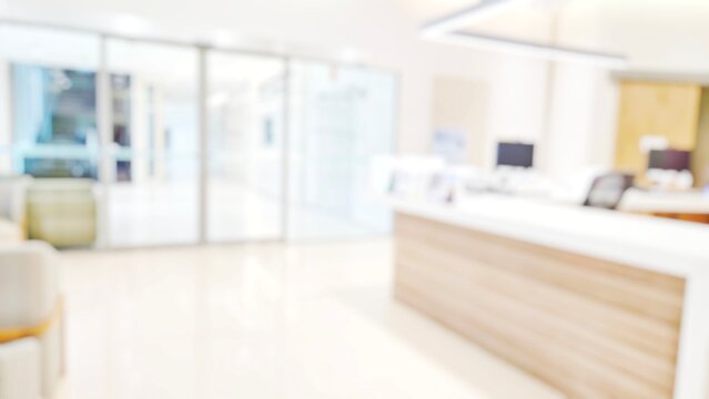 Blur abstract background of corridor in clean hospital. Blurry view of aisle in office with light floor. Defocus walkway in white light building hall with patient registration at reception desk.