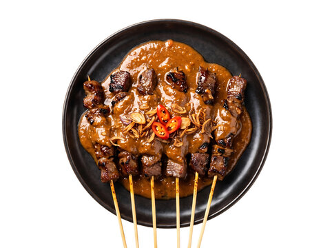Beef satay skewers topped with rich peanut sauce and chili on a dark plate isolated element on transparent background.
