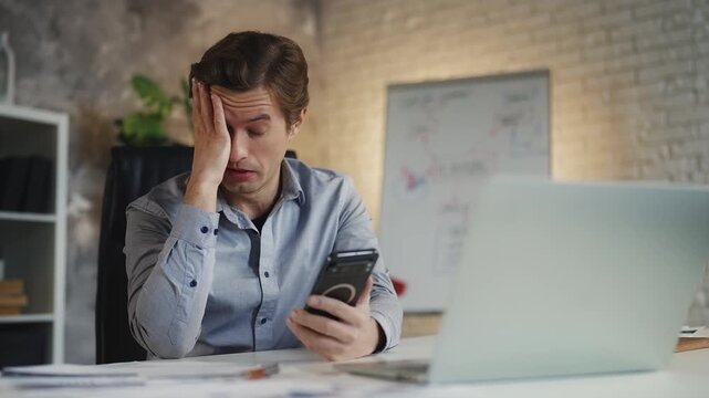 Sad businessman checking account balance on phone, victim of financial scheme