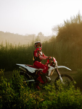 Woman rider on a dirt bike during a sunny morning in the countryside field wearing safety gear