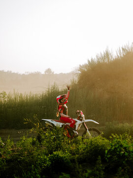 Motocross rider celebrating success on a dirt bike during sunset in a dusty field landscape