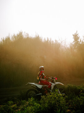 Woman sitting on a motocross bike in the woods during a sunny afternoon with golden dust in the air