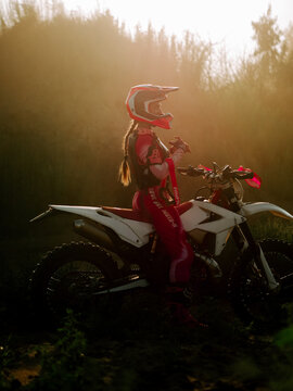 Woman riding a motocross bike during a sunny golden hour in the forest with protective gear