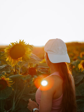 Young woman standing in a sunflower field while watching the bright sunset during a summer evening