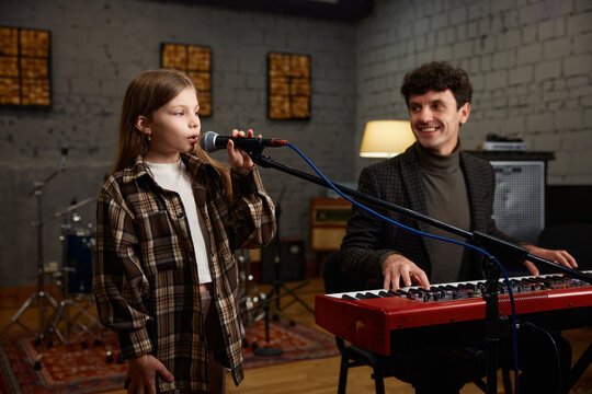 Coach accompanies girl vocalist at mic during focused studio rehearsal