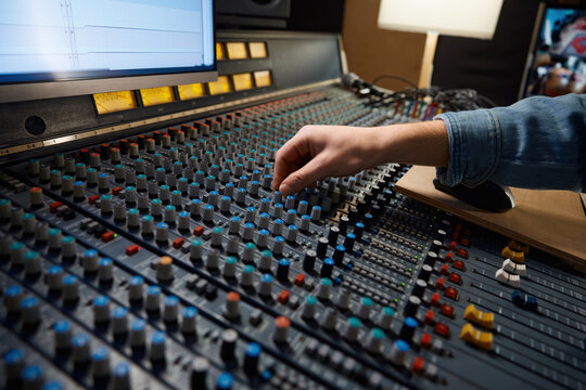 Detailed view of operators manipulating analog mixing knobs during session
