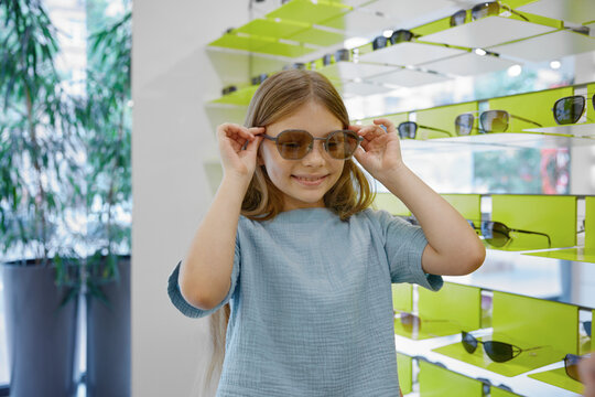 Young girl trying on fashionable glasses in a store setting with joyful expression