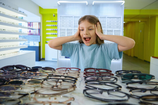 Girl enthusiastically trying on different spectacles amidst colorful store
