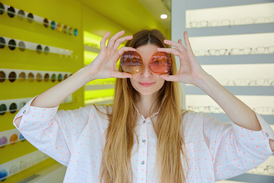 Happy woman displaying sunglasses amidst colorful shop