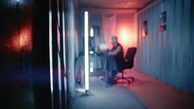 A cinematic dystopian technology scene showing a programmer working inside a custom industrial container filled with digital equipment.