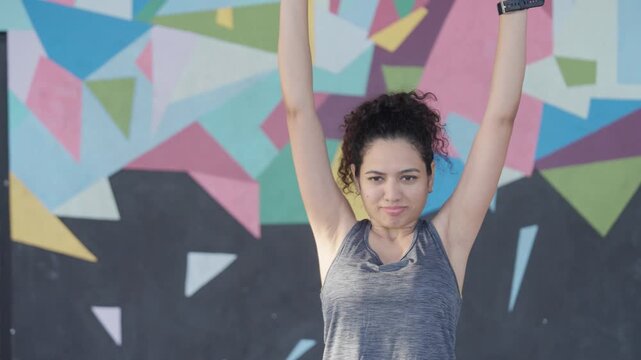 South Asian female athlete performs standing dumbbell shoulder presses in a modern indoor gym. Mid close shot with a subtle arc camera movement. Collection: WORKOUTSERIES2026.