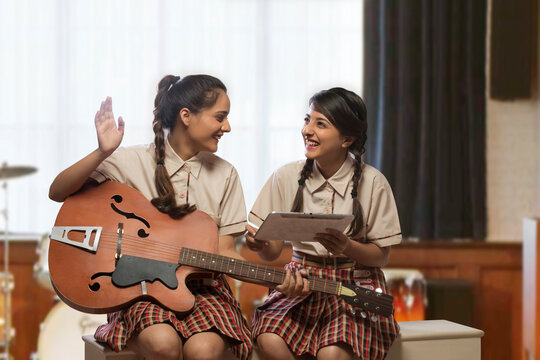 Two happy teenage school girls having fun learning to play guitar in the music room at school