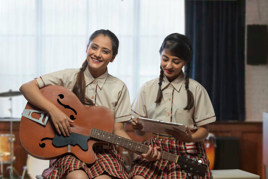 Two happy teenage school girls learning to play guitar in the music room at school